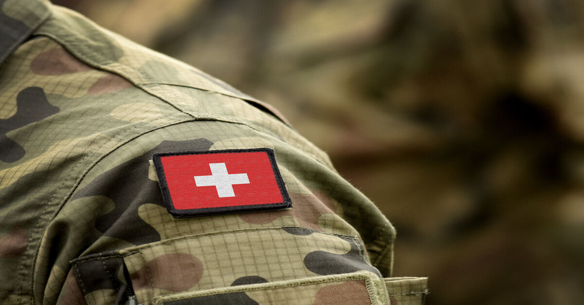 A close-up of the shoulder of a military uniform in green camouflage with a patch of the Swiss flag.