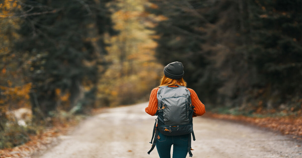 A behind shot of a traveler wearing an orange sweater, a black beanie, and a black rucksack.